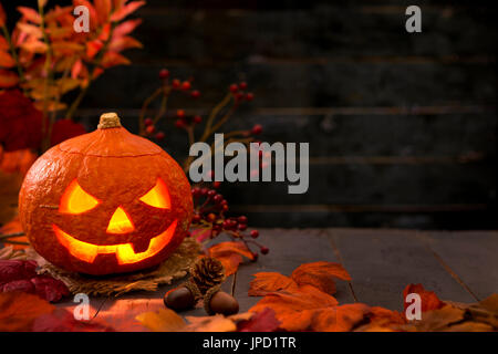 Brennen von Jack O'Lantern auf einem rustikalen Tisch mit herbstlichen Dekorationen, beleuchtet dunkel. Stockfoto