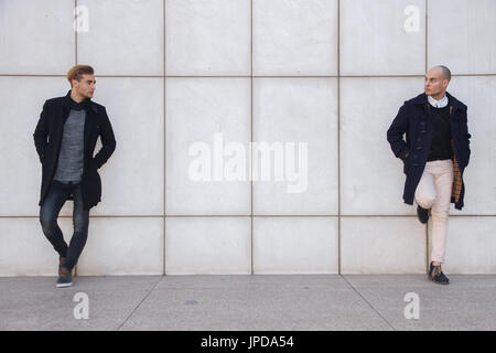 Zwei junge Unternehmer gekleidet in moderner und eleganter Kleidung eine weiße Wand gelehnt. Sie sind Geschäftspartner. Stockfoto