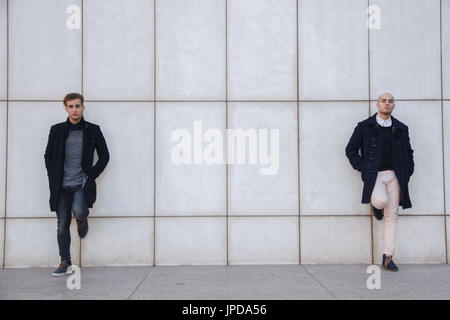 Zwei junge Unternehmer gekleidet in moderner und eleganter Kleidung eine weiße Wand gelehnt. Sie sind Geschäftspartner. Stockfoto