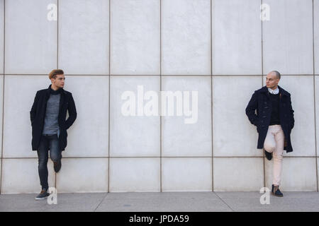 Zwei junge Unternehmer gekleidet in moderner und eleganter Kleidung eine weiße Wand gelehnt. Sie sind Geschäftspartner. Stockfoto