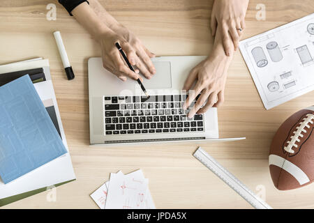 Paar ist die Verwendung eines Laptops auf den Holztisch in der Werkstatt. Rund um den Laptop gibt es Zugluft, Entwürfe, Notebook und Bücher, Marker und ein Bleistift, r Stockfoto
