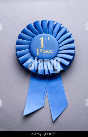 Blauen gefalteten Band Meisterschaft Rosette für den ersten Platz mit gold Text auf grau in ein Konzept von Sport, Wettbewerb und Erfolg liegen