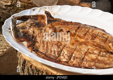 Nahaufnahme von frischem Fisch mit Sauce auf einer offenen Flamme Grill auf große weiße Platte gekocht. Gebratener Fisch mit Spice und Sauce am Grill zubereitet auf hölzernen Bac Stockfoto