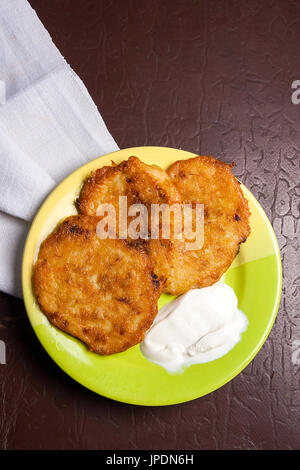 Hausgemachte Kartoffelpuffer. Kartoffel Krapfen mit Fleisch und Sauerrahm auf grüne Platte auf Vintage braun dunkel. Herkömmlichen Belarussisch und Ukraini Stockfoto