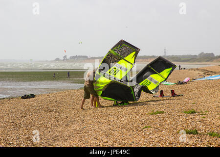 Ein paar junge Männer Kampf gegen eine steife Brise, bereiten Sie ihre Para-Gleiter für einen Nachmittag Sport am Strand in Titchfield Hampshire in th Stockfoto