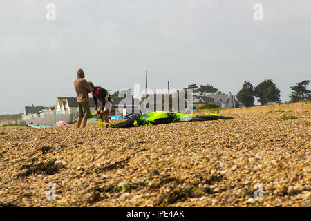 Ein paar junge Männer Kampf gegen eine steife Brise, bereiten Sie ihre Para-Gleiter für einen Nachmittag Sport am Strand in Titchfield Hampshire in th Stockfoto