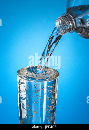 Wasser in ein Glas gießen, über blauem Hintergrund Stockfoto