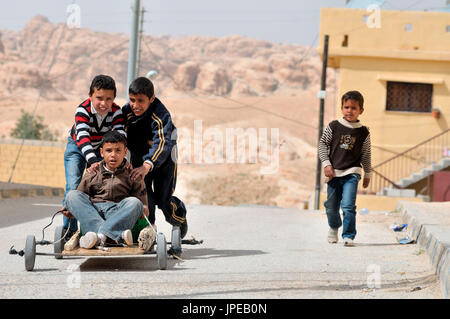 In einer Straße in der Nähe von Petra, Jordanien, Kinder spielen und laufen entlang einer Straße in einem Wagen von selbst gebaut Stockfoto