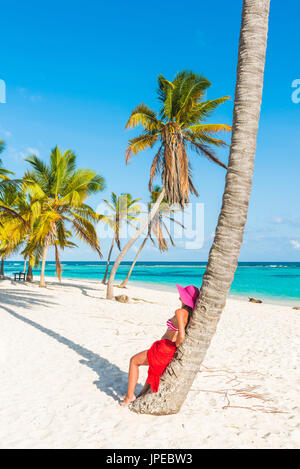 Canto de la Playa, Saona, East National Park (Parque Nacional del Este), Dominikanische Republik, Karibik. Schöne Frau mit roten Sarong entspannen auf den palmengesäumten Strand (MR). Stockfoto