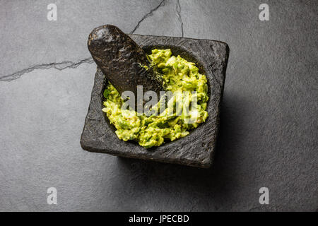 Traditionelle lateinamerikanische mexikanische Sauce Guacamole im Steinmörser, Schiefer grau hinterlegt. Stockfoto