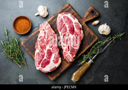 Rohes Schweinefleisch Schnitzel für Grill BBQ mit Kräutern auf Holzbrett, Schiefer Hintergrund, Ansicht von oben Hacken. Stockfoto