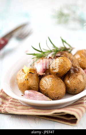 Ofen gebackene Kartoffeln oder Pellkartoffeln mit gebackenem Knoblauch und Rosmarin auf einem weißen ovalen Teller Stockfoto