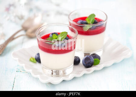 Köstliche italienisches Dessert Panna Cotta mit Himbeersauce und frischen Heidelbeeren serviert für zwei Personen in kleine transparente Gläser Stockfoto