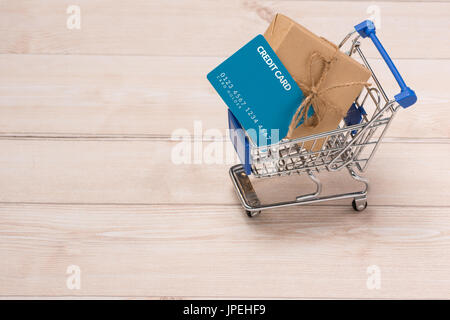 Kreditkarte und Einkaufswagen mit Geschenkbox verpackt mit Papier Kraft auf Tisch. Stockfoto