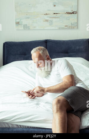 älteren bärtigen mit Smartphone auf Bett liegend Stockfoto