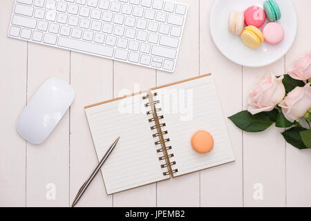 Weißer Schreibtisch mit bunten Macarons, Tastatur und offene Notebook. Stockfoto