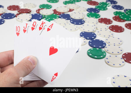 Spieler, die im Besitz einer Hand Poker-Karten zeigen gerade Royal Flush Poker über eine Tabelle mit verstreuten Casino-Chips zu gewinnen Stockfoto