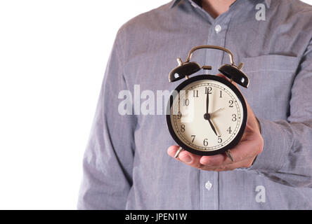 Mann hält ein Retro-Wecker mit der Zeit von der Arbeit oder Geschäft in einer Nahaufnahme auf 05:00 in ein Konzept der Heimatzeit festgelegt Stockfoto