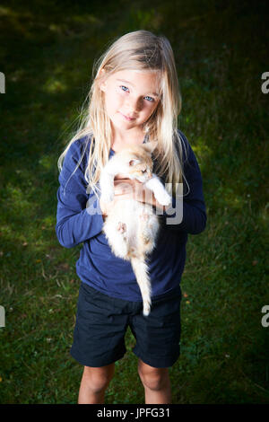 Outdoor Portrait von niedlichen kleinen Kind blondes Mädchen mit kleinen Kätzchen, Mädchen spielen mit Katze auf grünen Hintergrund Stockfoto