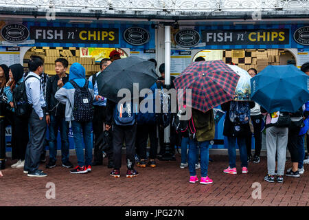 Brighton, UK. 2. August 2017. Großbritannien Wetter. Eine Gruppe von jungen chinesischen Touristen Warteschlange im Regen, Fish &amp; Chips auf Brighton Seafront, Brighton, East Sussex, UK zu kaufen. Bildnachweis: Grant Rooney/Alamy Live-Nachrichten Stockfoto