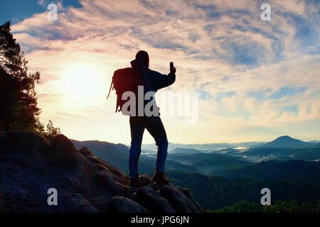 Tourist mit Rucksack nimmt Fotos mit Smart Phone auf dem felsigen Gipfel. Verträumt fogy Tal Stockfoto