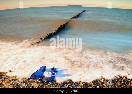 Maske mit blauen Flossen zum Schnorcheln bereit für den Einsatz auf steinigen Strand von hölzernen Wellenbrecher. Wellig Meeresspiegel. Stockfoto