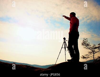 Naturfotograf mit Stativ auf Klippe und denken. Verträumte Kauz Landschaft, orange nebligen Sonnenaufgang in einem wunderschönen Tal unten Stockfoto