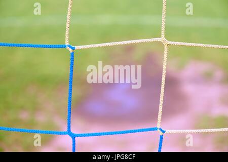 Blick durch Fußball Tor zum Wasser und Mude in armen Fußballplatz. Beschädigte Rasen in Outdoor-Fußballstadion Stockfoto