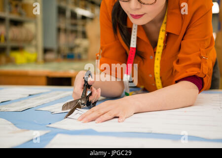 Nahaufnahme von attraktiven schöne junge Schneider entlang Design Entwurf Rand mit einer Schere schneiden neue Kleidung Proben auf Arbeitstisch in Fabrik Muster depa Stockfoto