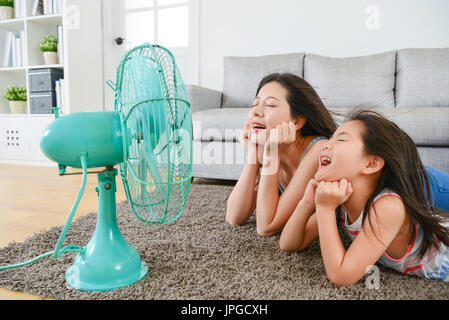 angenehm Mutter mit jungen Töchterchen liegend am Boden des Wohnzimmers und von Angesicht zu elektrischen Ventilator bläst kühlen Wind zusammen im Sommer zu genießen. Stockfoto