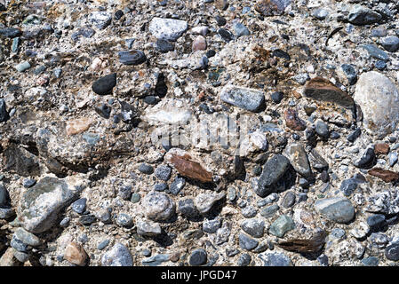 Nahaufnahme einer sehr abgenutzt und verwitterten Betonwand mit Felsen ragen aus dem Mauerwerk. Stockfoto