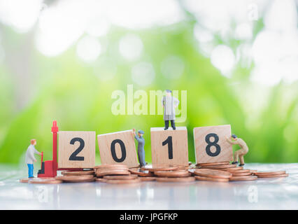 Winzige Miniaturmodell des Arbeitens harte Arbeiter stehend auf einem Haufen von Münzen und Holz-Nummer 2018 Hintergrund als Investition, Leistung und partne Stockfoto