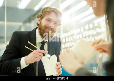 Porträt des modernen bärtigen Geschäftsmann glücklich lächelnd, während chinesische Essen im Büro Mittagessen mit Kollegen teilen Stockfoto