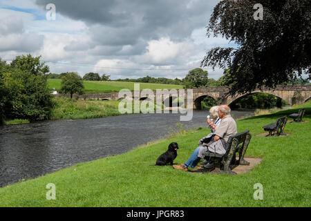 Ein älteres Paar entspannende mit ihren Hund am Ufer des Flusses Ribble an edisford Brücke in der Nähe von Clitheroe in Lancashire Stockfoto