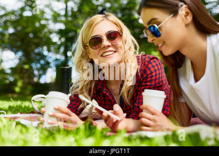 Porträt von zwei schöne junge Mädchen Picknick im sonnigen Park Handauflegen Decke mit Kaffeetassen Stockfoto