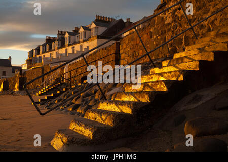 Konkrete Schritte in die goldenen Strahlen von einem Sonnenuntergang am Strand entlang in Lower Largo, Fife, Schottland. Stockfoto