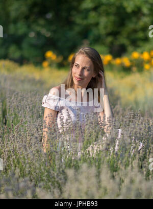 Schöne Frau im sonnigen Tag rosa Kleid und sitzen in frischer Lavendel Feld, Schönheit der Natur genießen Stockfoto