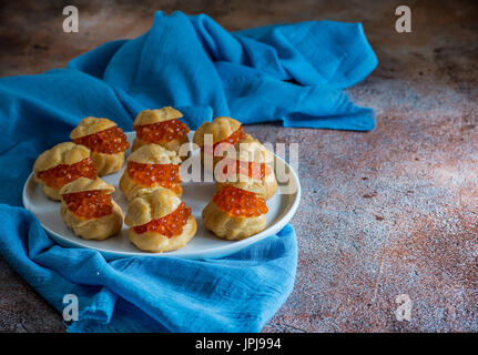 Hausgemachten Profiteroles gefüllt mit rotem Kaviar auf weißen Teller. Natürliches Licht, niedrigen Winkel, selektiven Fokus Stockfoto