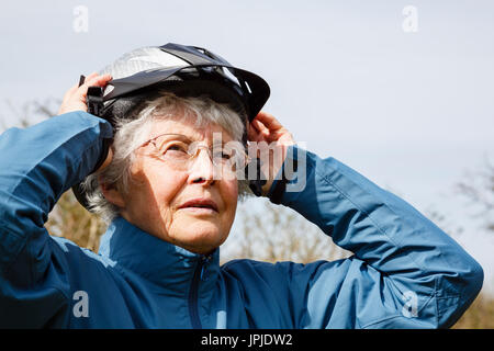 Aktive ältere ältere Frau Rentner auf einen Radhelm Vorbereitung einer Radtour und einer gesunden Verstand zu halten zu gehen. England Großbritannien Großbritannien Stockfoto