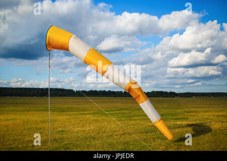 Gestreift orange-weiße Windsack gegen blauen Himmel mit Wolken und Feld Gras. Stockfoto
