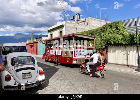 Touristische Laufkatze hinauf der Straße gefolgt von Motorrad paar mit Kind, auch Volkswagen Käfer. Oaxaca de Juárez, Oaxaca, Mexiko Stockfoto