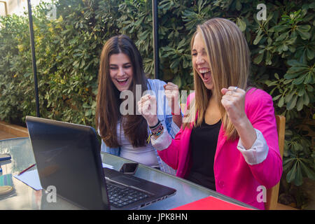 Gruppe von zwei jungen Mädchen euphorische Unternehmer für die Ergebnisse in Ihrem Unternehmen erhalten. Sie sitzen auf der Terrasse Tisch arbeiten. Stockfoto