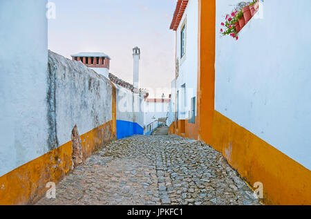 Der Spaziergang entlang der alten weißen Mauern der Stadt, geschmückt mit hellen gelben Streifen und Blumen in Töpfen, Obidos, Portugal. Stockfoto