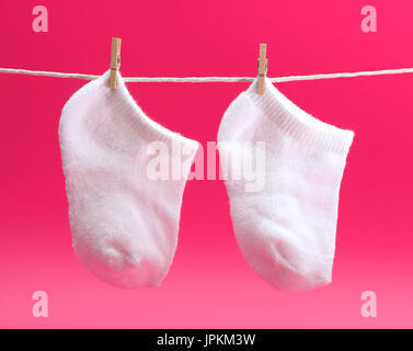 Ein paar weiße Babysocken auf einer Wäscheleine Stockfoto