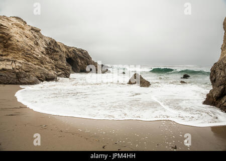 am Ufer zwischen Felsen mit Stein in Mitte und eine Welle im Ozean Stockfoto