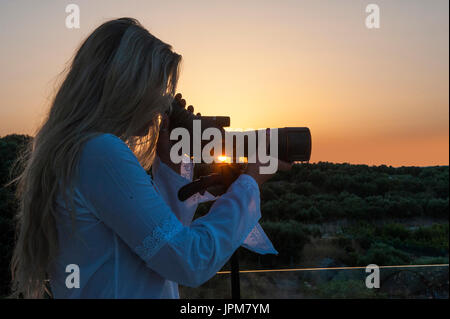 Ein hübsches Mädchen schaut durch ein Teleskop bei Sonnenuntergang Stockfoto