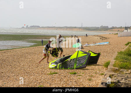 Ein paar junge Männer Kampf gegen eine steife Brise, bereiten Sie ihre Para-Gleiter für einen Nachmittag Sport am Strand in Titchfield Hampshire in th Stockfoto