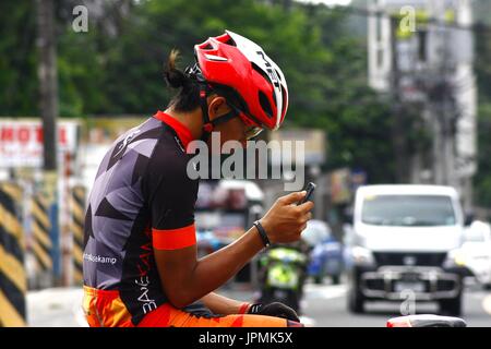 ANTIPOLO CITY, Philippinen - 30. Juli 2017: Ein Biker eine Pause auf einem Bürgersteig und nutzt sein Smartphone. Stockfoto