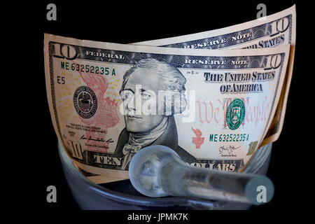 Amerikanische 20-Dollar-Noten wird mit einem Stößel im Mörser Glas zerschlagen. Stockfoto