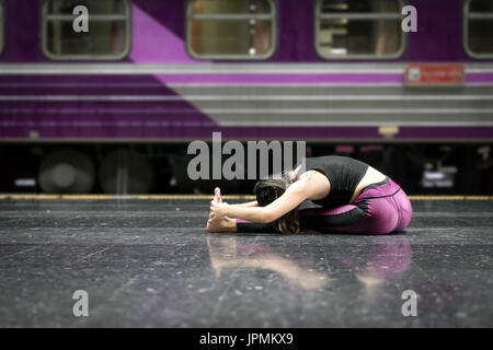 Flexibles Mädchen, das Yoga macht, posiert auf dem Boden eines Bahnhofs, das Fitnesskleidung trägt Stockfoto